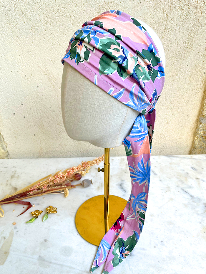 Floral pink and purple head scarf wrapped around a mannequin head on a stand, showcasing a bold summer print.