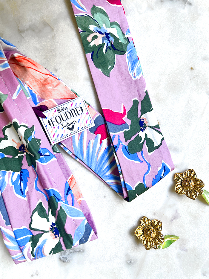 Pastel pink and purple floral tie on a marble surface with a small brand tag nearby.