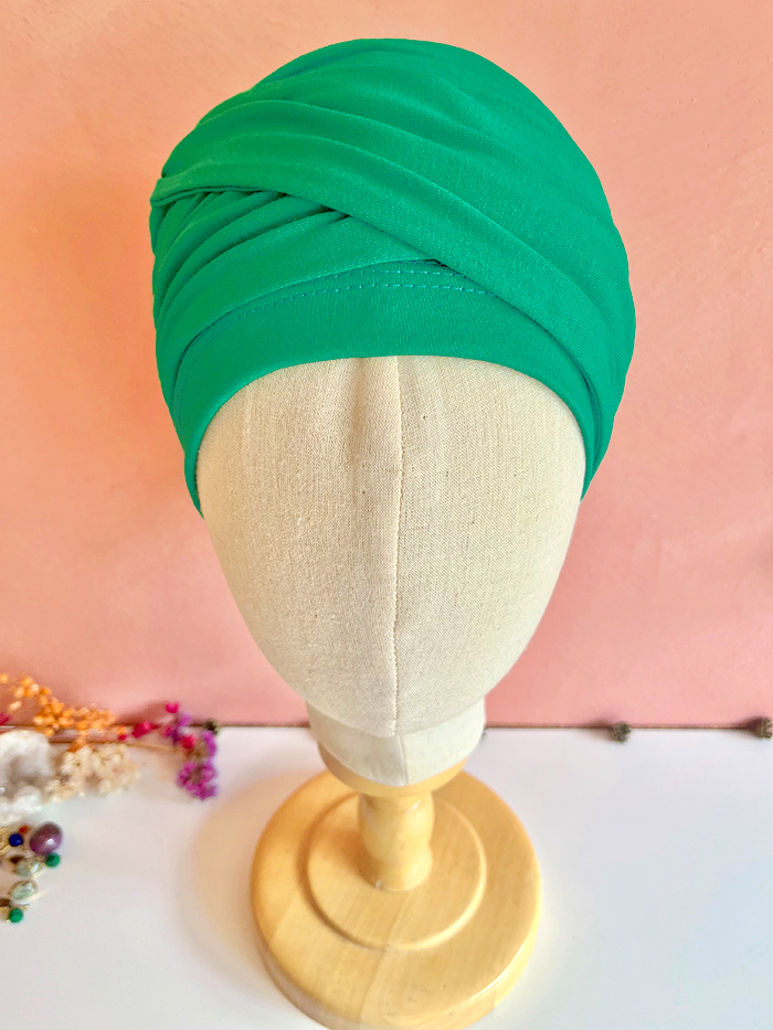 Green turban headwrap on a beige display mannequin against a pink wall.