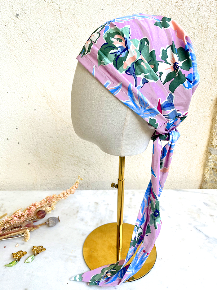 Pink floral headscarf wrapped around a mannequin head on a gold stand, with a long tie hanging down the side.