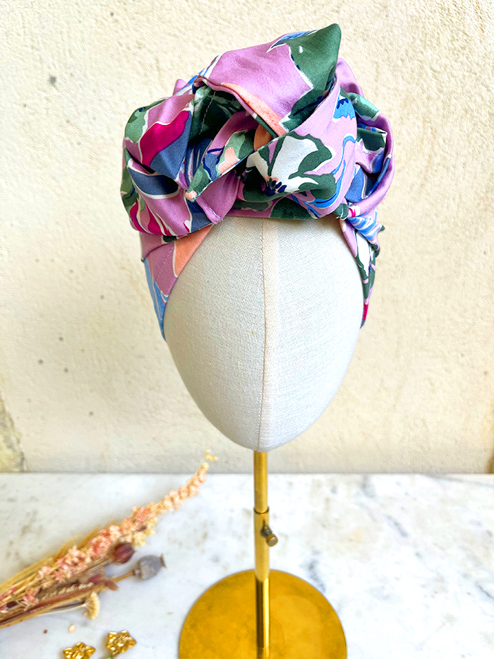 Colorful patterned head wrap tied around a beige mannequin head on a gold stand in a fashion display.