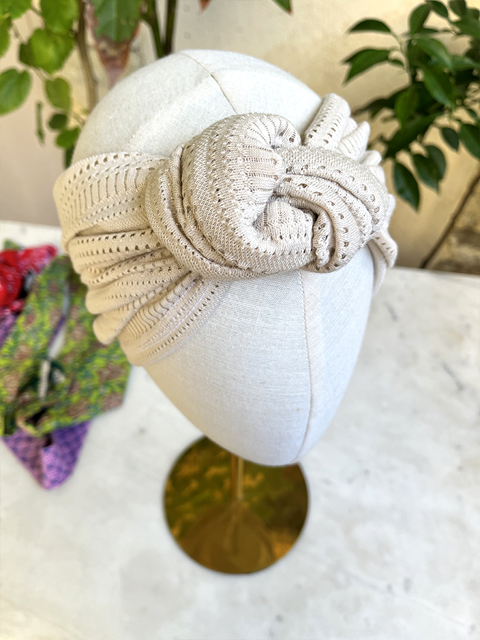 Beige knitted turban-style headwrap tied in a knot on a mannequin head