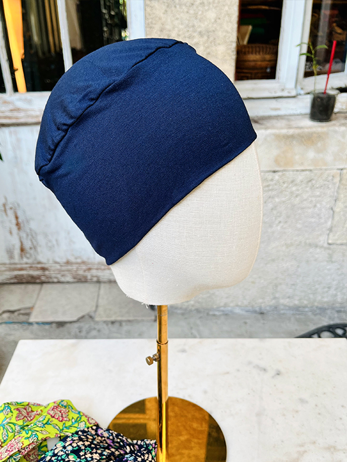 Navy blue slouchy cap displayed on a beige mannequin head mounted on a brass stand in an outdoor shop setting.