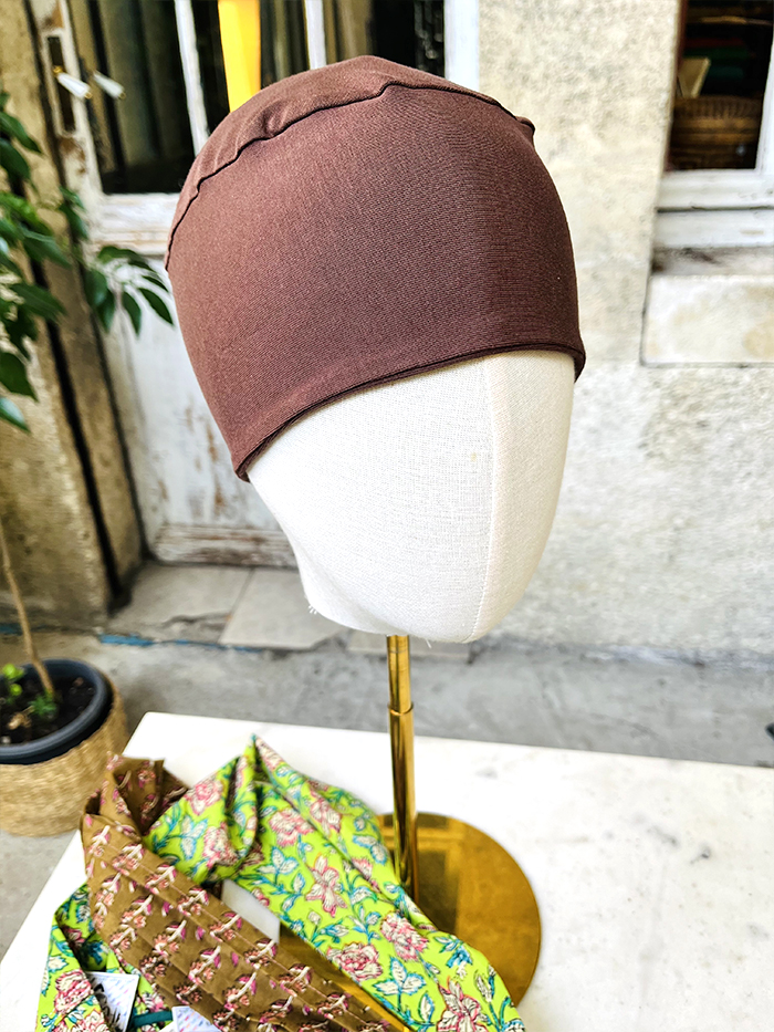 Brown fabric headwrap on a dress-form mannequin outdoors, with colorful patterned fabrics at the base.