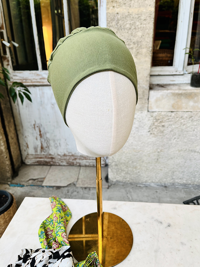 Olive green headscarf draped over a mannequin head on a gold display stand outdoors.