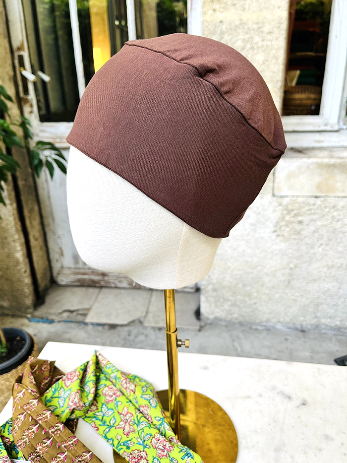 Brown fabric head wrap on a white mannequin head outdoors, with patterned scarves nearby.
