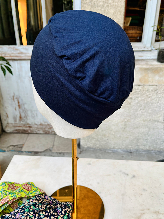 Navy blue fabric head covering displayed on a beige mannequin head atop a gold stand, indoors.