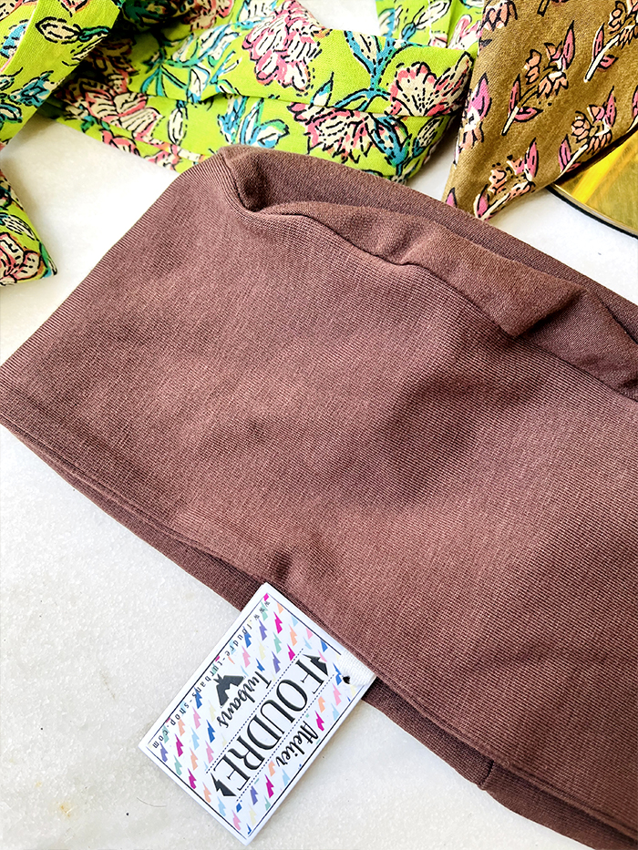 Brown folded fabric with a white clothing tag, colorful floral fabrics visible in the background.