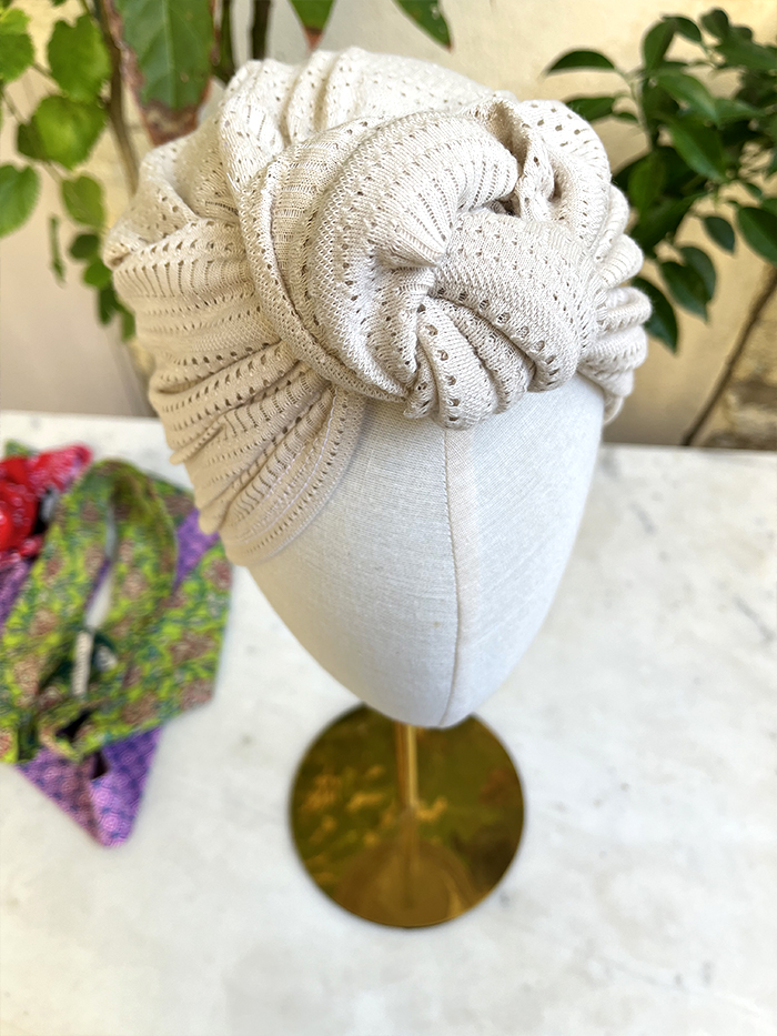 Beige knitted turban-style headwrap displayed on a dress form mannequin, showcasing ribbed texture and folds