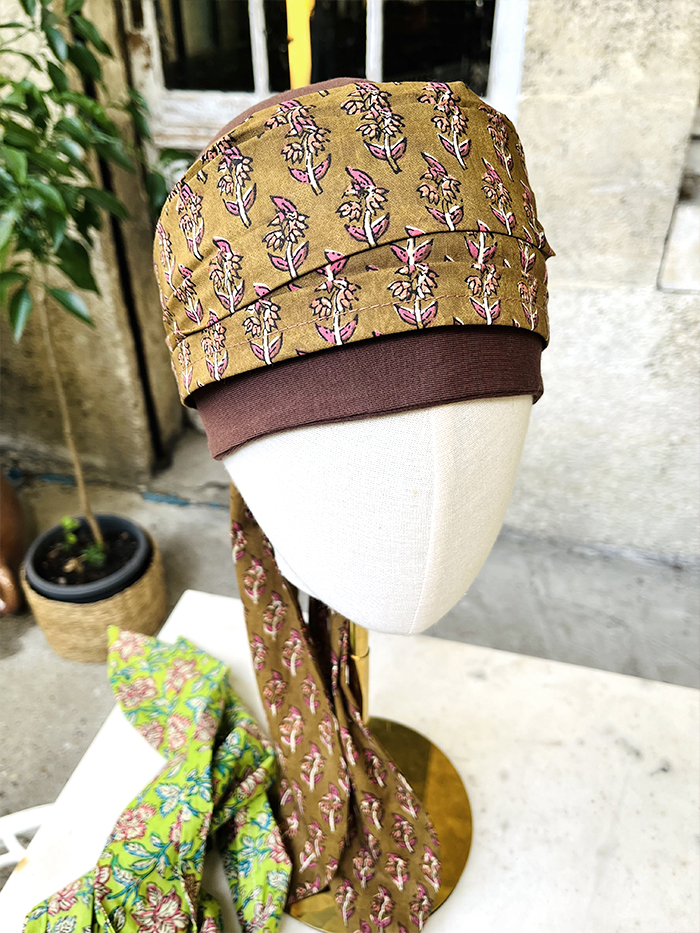 Beige-brown cap with pink floral pattern on a display head, paired with a matching scarf draped nearby outdoors.