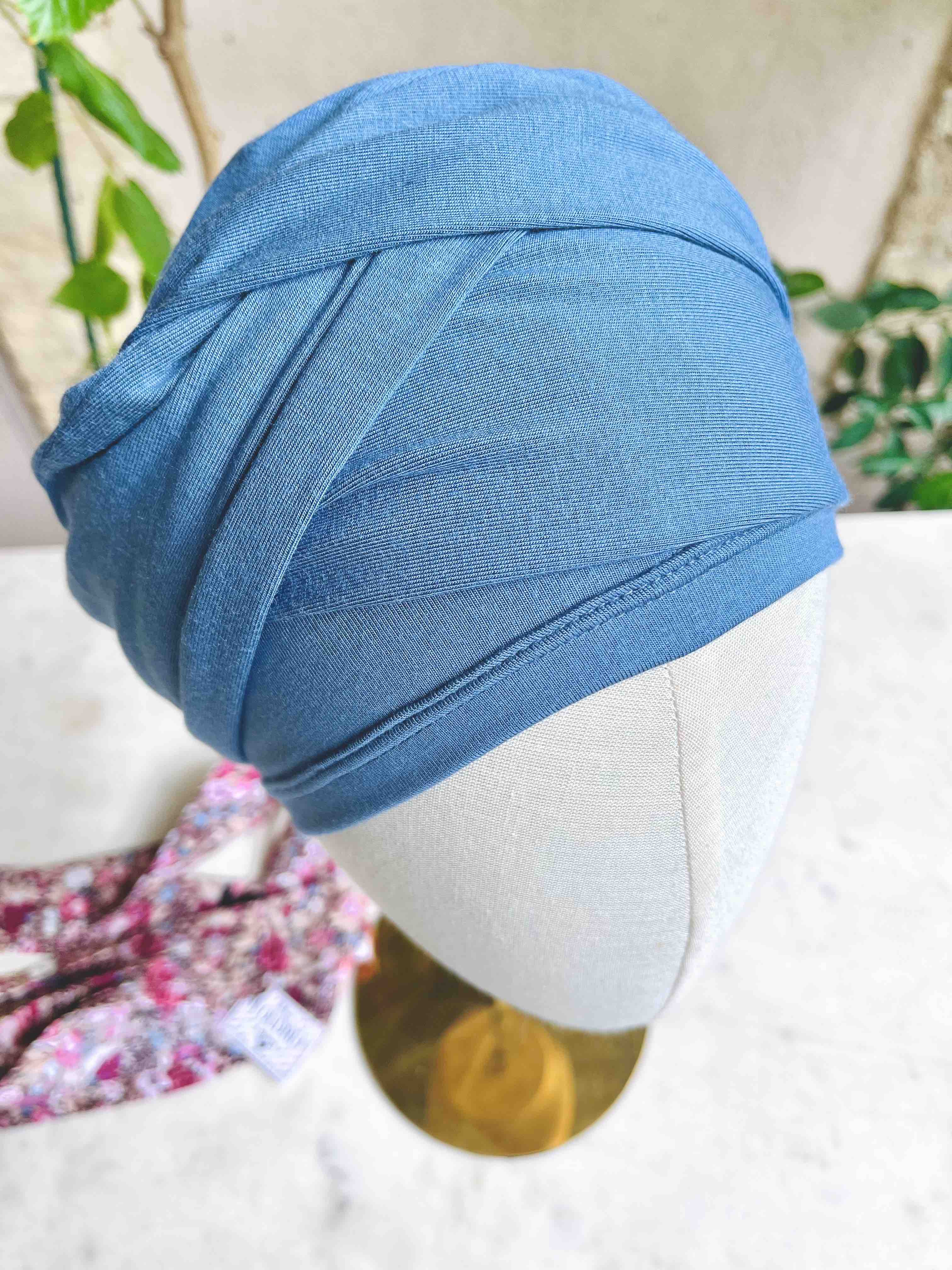 Blue denim turban-style hat displayed on a light mannequin head outdoors.