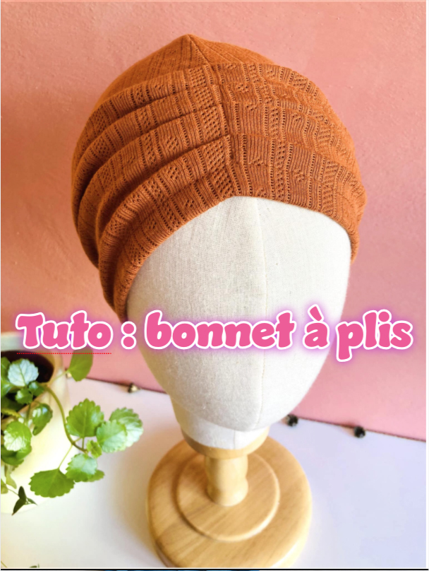 Brown knitted turban-style hat on a dress form against a pink wall, with text overlay 'Tuto : bonnet à plis' indicating a pleated hat tutorial.